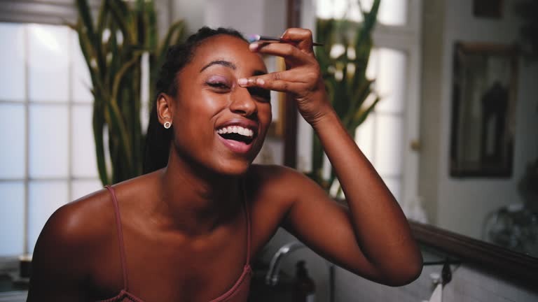 cheerful young female make up expert applying eyeshadow while vlogging in bathroom at home